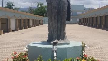 Una estatua de una mujer sobre un pedestal, con un borde amarillo y flores rojas al frente.