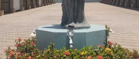 A statue of a woman on a pedestal with a yellow border and red flowers in front.