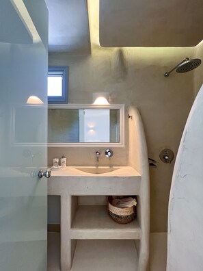 A bathroom with a built-in sink, a mirror, and a shower area. - Palmariva Villas (Santorini)