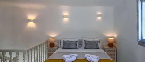 Un dormitorio con una cama blanca, dos mesitas de noche con lámparas, una ventana y una escalera.