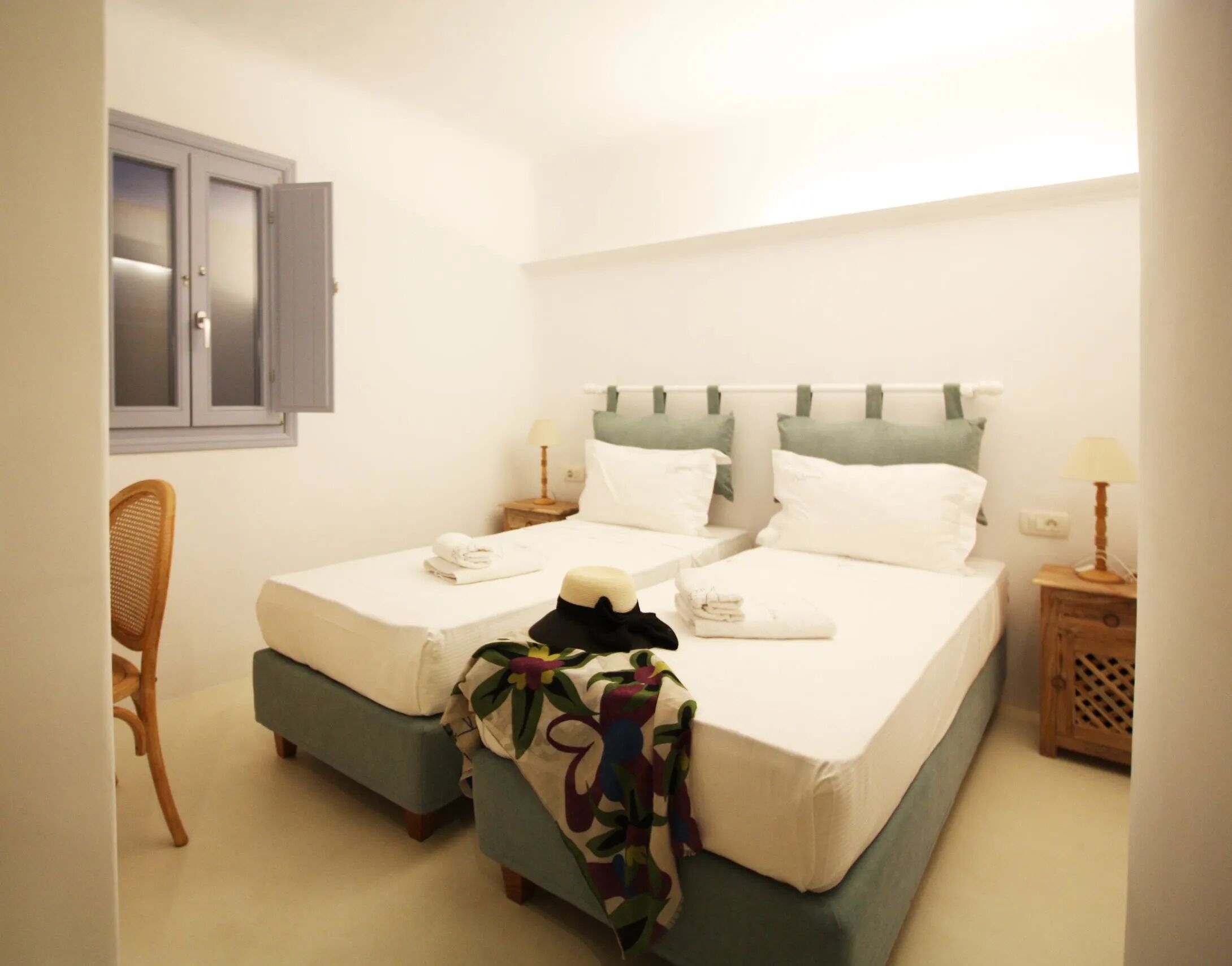 A double bed with a green headboard, two bedside tables with lamps, a chair, and a window with frosted glass.