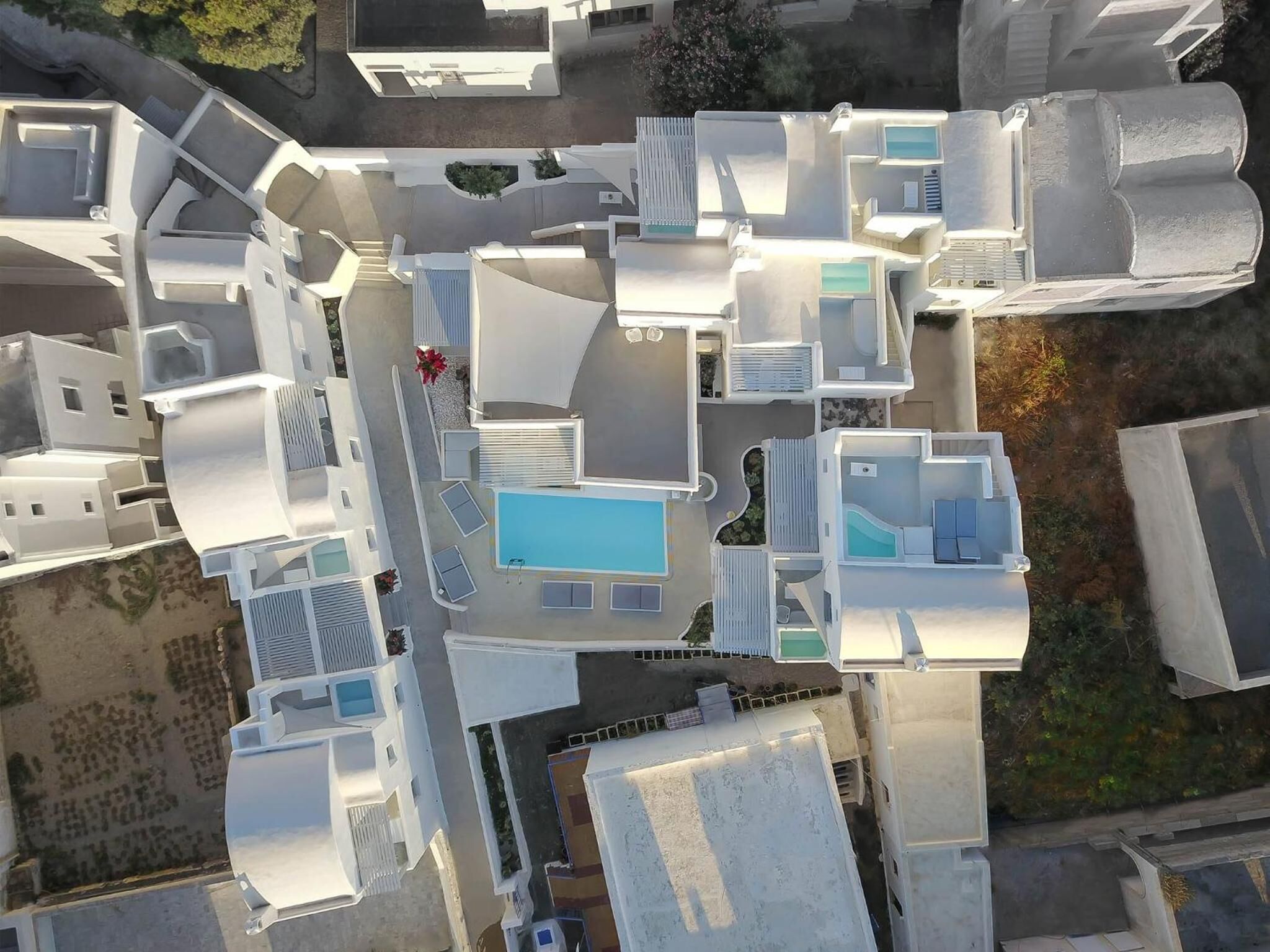 An aerial view of a residential area with multiple buildings, including a house with a swimming pool, a fenced garden, and a small red flower bed.