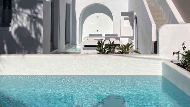 A modern white building with a pool, a staircase, and a small seating area with plants. - Palmariva Villas (Santorini)