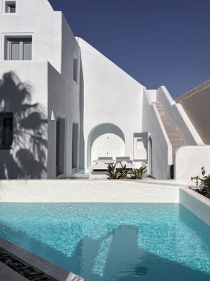 A modern white building with a pool, a staircase, and a small seating area with plants.