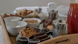 A breakfast tray with various food items, a coffee pot, and a window with pink flowers. - Palmariva Villas (Santorini)