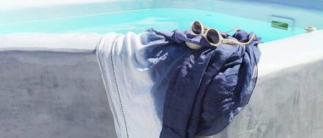Une piscine avec une eau d’un bleu limpide, un bord en béton et une serviette bleue sur laquelle reposent des lunettes de soleil.