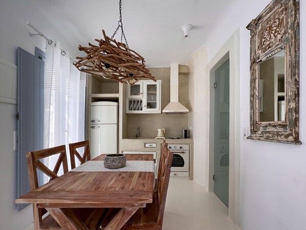 A dining area with a wooden table and chairs, a hanging light fixture, a kitchen with cabinets and appliances, and a mirror on the wall.