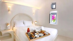 A neatly made bed with a tray of breakfast items, a bedside lamp, and a window with a view of flowers. - Palmariva Villas (Santorini)