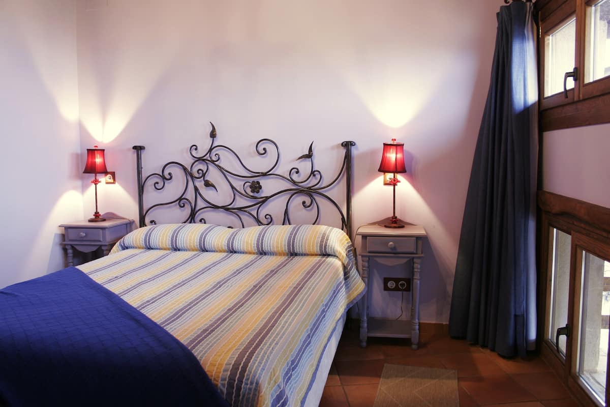 A neatly made bed with striped bedding, two bedside tables with lamps, and a window with curtains.