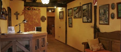 A cozy interior with a wooden reception desk, a bench with cushions, and a hallway with framed pictures on the walls.