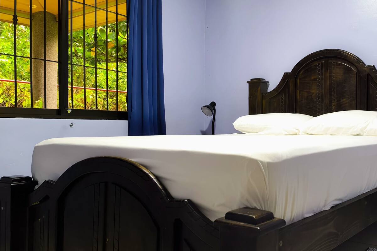 A neatly made bed with white linens, a wooden headboard, and two bedside lamps on a nightstand.