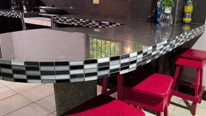 A kitchen counter with a checkered tile border, a red stool, and a potted plant.