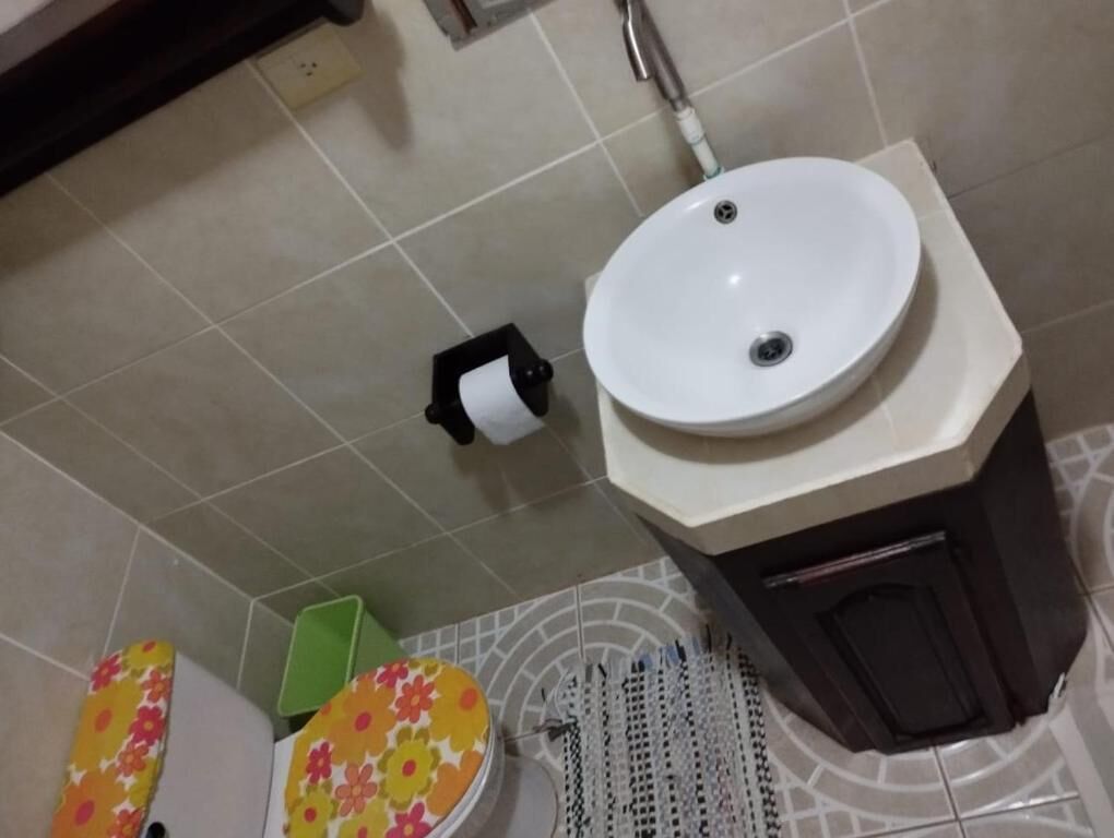 A bathroom with a white sink, a toilet paper holder, and a patterned mat.