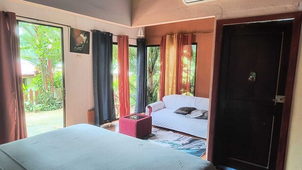 A room with a bed, a sofa, and a small table. There is a door and a window with curtains.