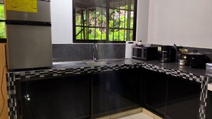 A modern kitchen with a black and white tiled backsplash, a stainless steel refrigerator, a microwave, a coffee maker, and a window with a view of greenery.