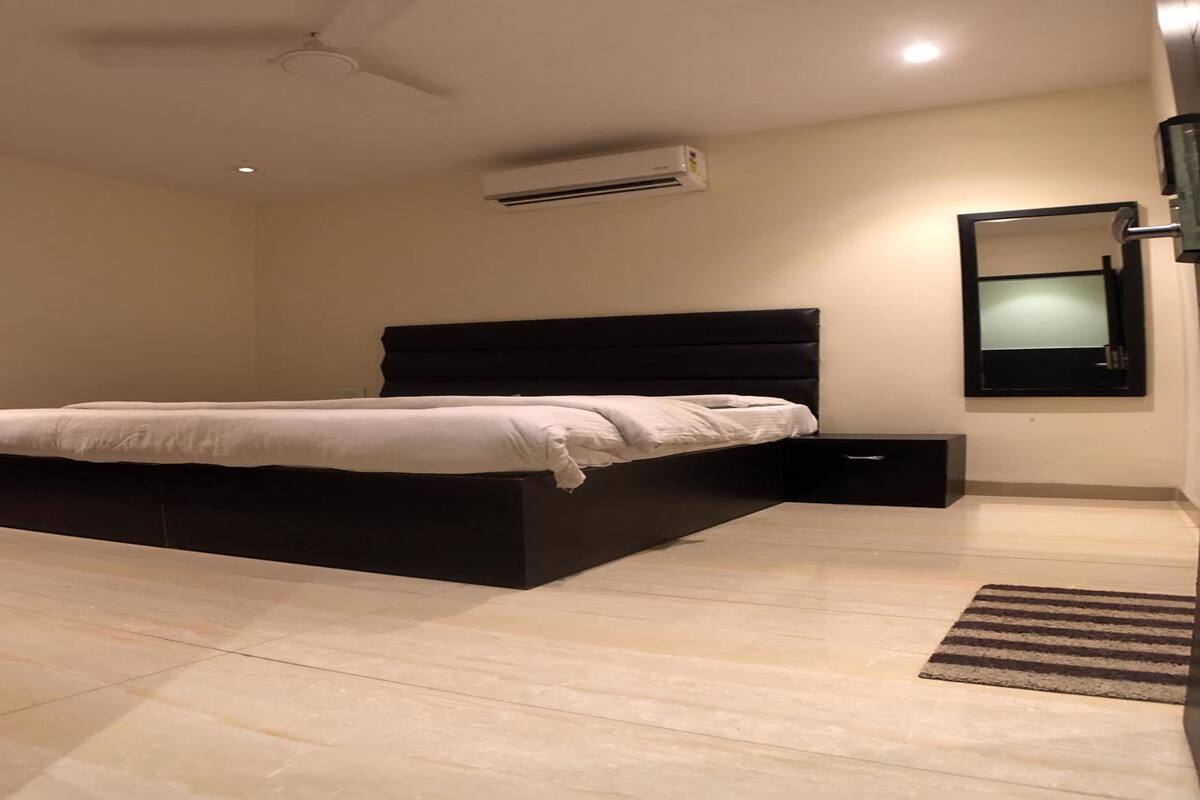 A modern bedroom with a large bed, a nightstand, a wall-mounted TV, and an air conditioning unit.
