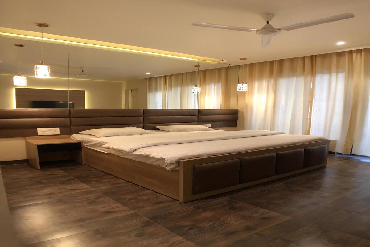 A modern bedroom with a large bed, bedside tables, a ceiling fan, and a large window with curtains.