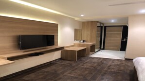 A modern hotel room with a flat-screen TV mounted on a wooden wall, a small wooden desk, a mirror, and a sliding door closet. - Solitaire Hotel (New Delhi)
