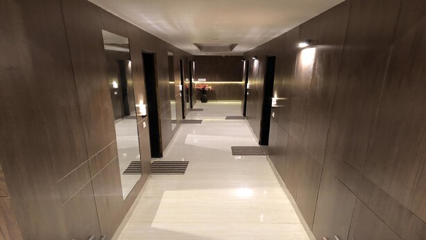 A modern, well-lit hallway with a marble floor and metallic walls, leading to a reception area with a vase of flowers. - Solitaire Hotel (New Delhi)