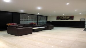 A modern living room with a sectional sofa, a coffee table, and a large window with curtains. - Solitaire Hotel (New Delhi)