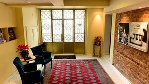 A room with a red patterned rug, a brick wall with framed pictures, and a large window with a geometric design. - Hotel Praça da Matriz (Porto Alegre)
