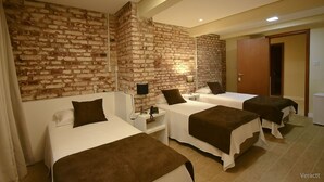 A hotel room with three beds, a brick wall, a wooden door, and a small bedside table with a lamp. - Hotel Praça da Matriz (Porto Alegre)