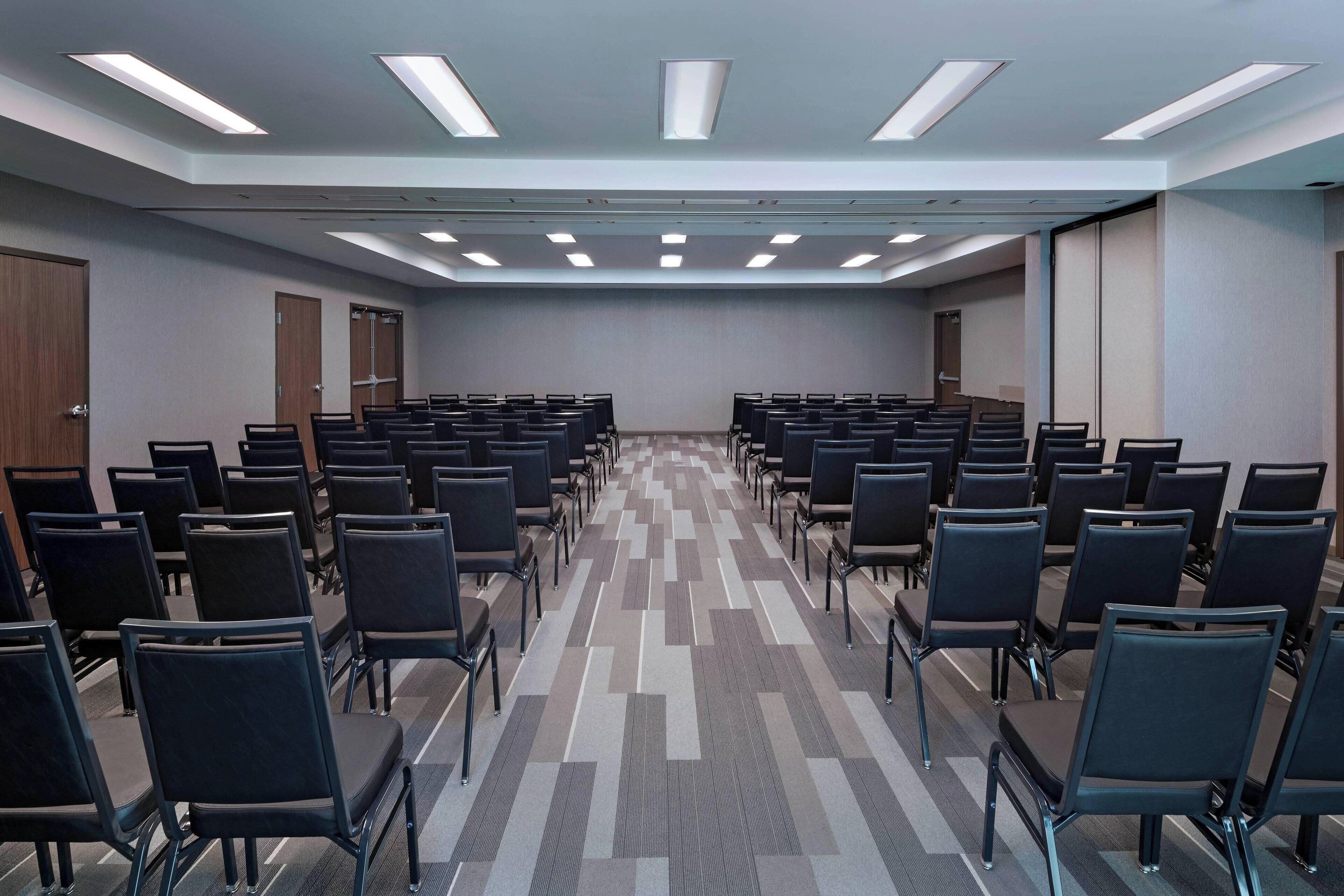 Ein Konferenzraum mit Reihen von Stühlen, einem gemusterten Teppich und eingelassenen Deckenleuchten.