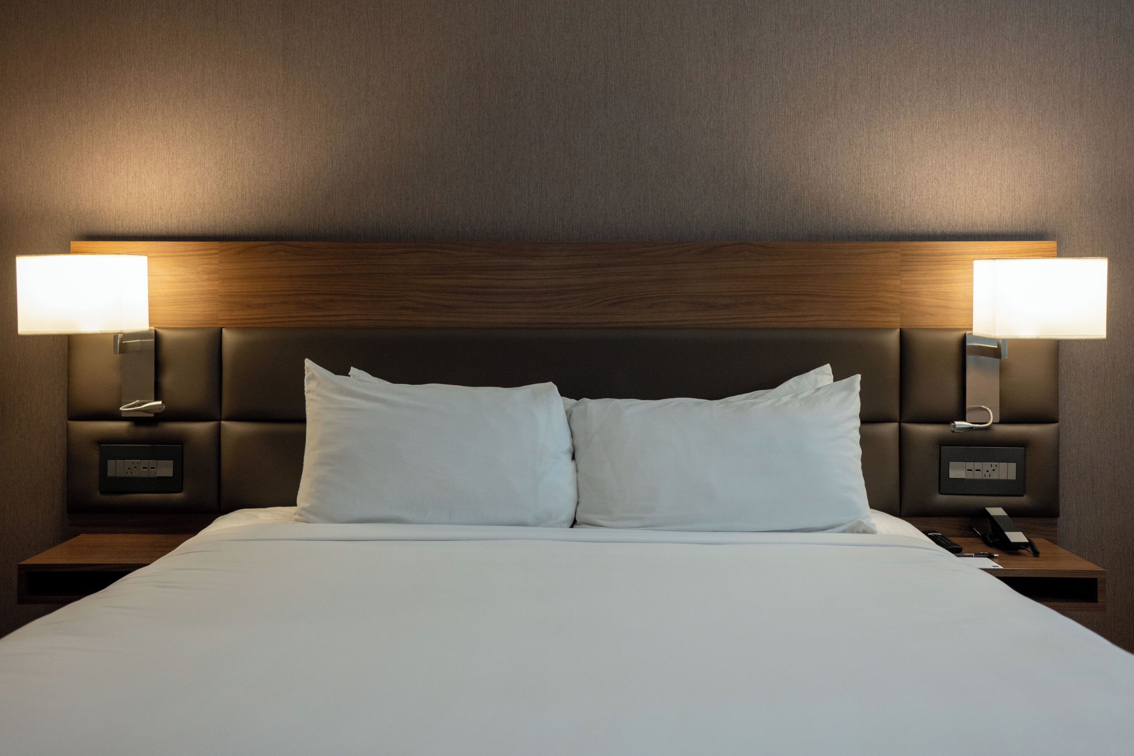 A hotel room with a large bed, two bedside lamps, and a wooden headboard.