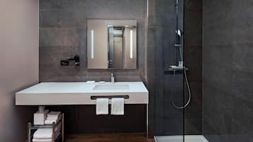 A modern bathroom with a large mirror, a white sink, and a glass-enclosed shower.