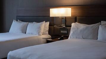 A hotel room with two beds, a nightstand, and a wall-mounted lamp.