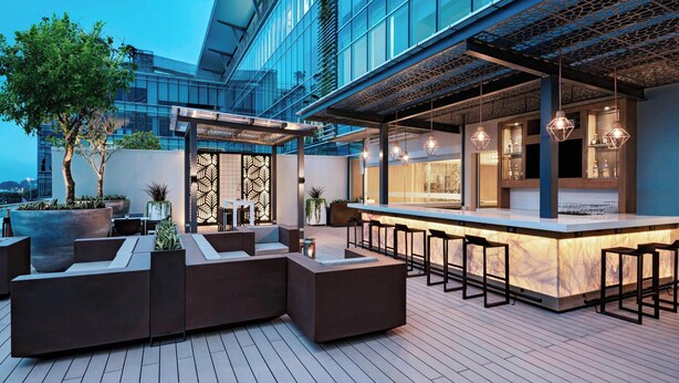 Un espace bar extérieur avec des sièges et une vue sur un bâtiment moderne.