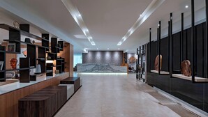 Un hall d’hôtel moderne avec un long comptoir d’accueil, des étagères en bois et un mur en pierre en arrière-plan.