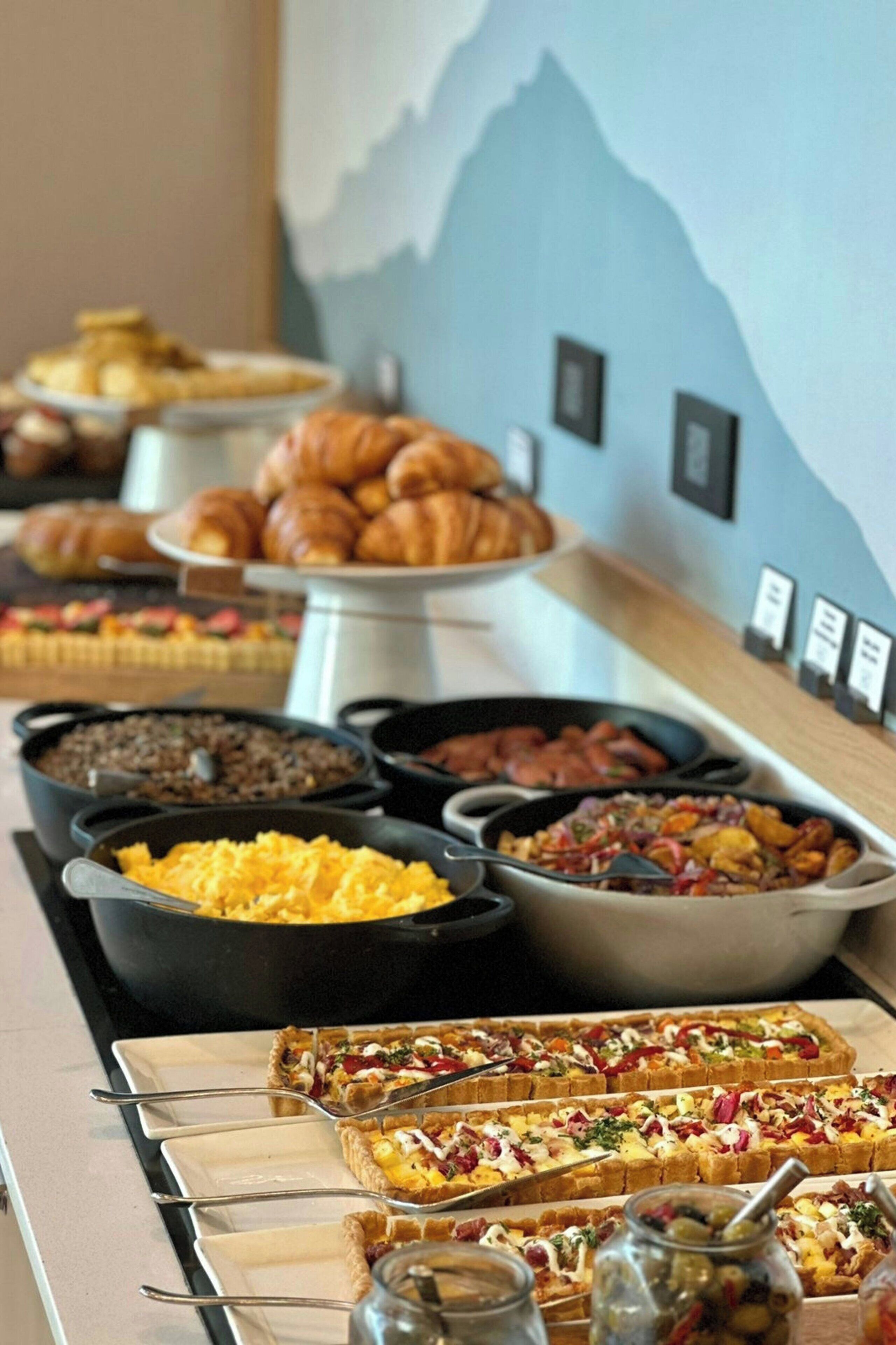 En buffet med forskellige retter, herunder røræg, pølser og bagværk.