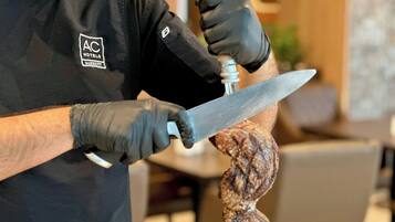 Una persona con delantal negro que lleva un logotipo, sosteniendo un cuchillo grande y un trozo de carne.
