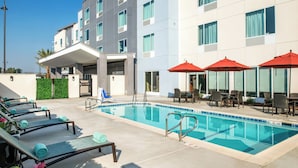 A hotel pool area with lounge chairs, red umbrellas, and a clear blue pool.