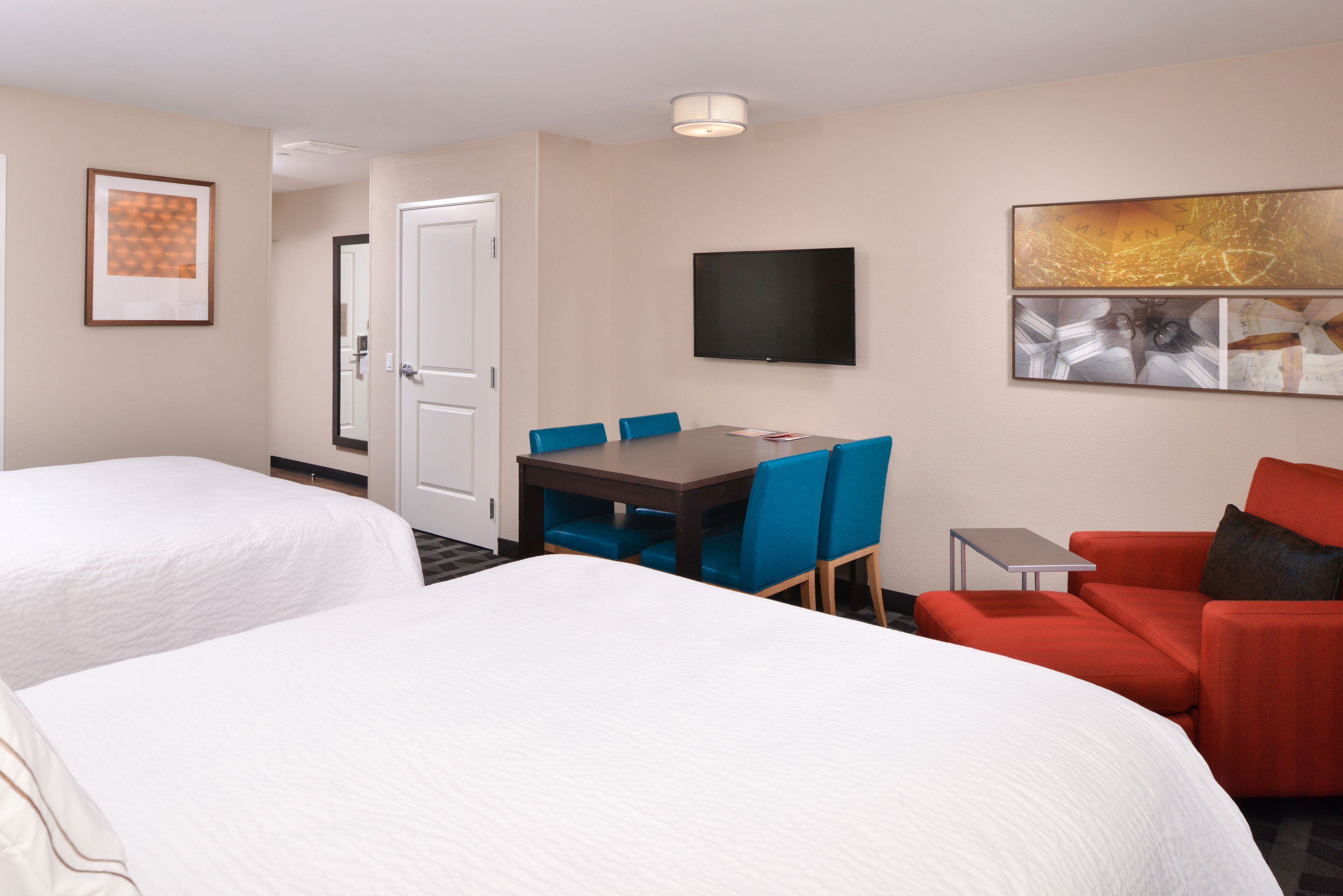 A hotel room with two beds, a dining table with chairs, a TV, and a red armchair.