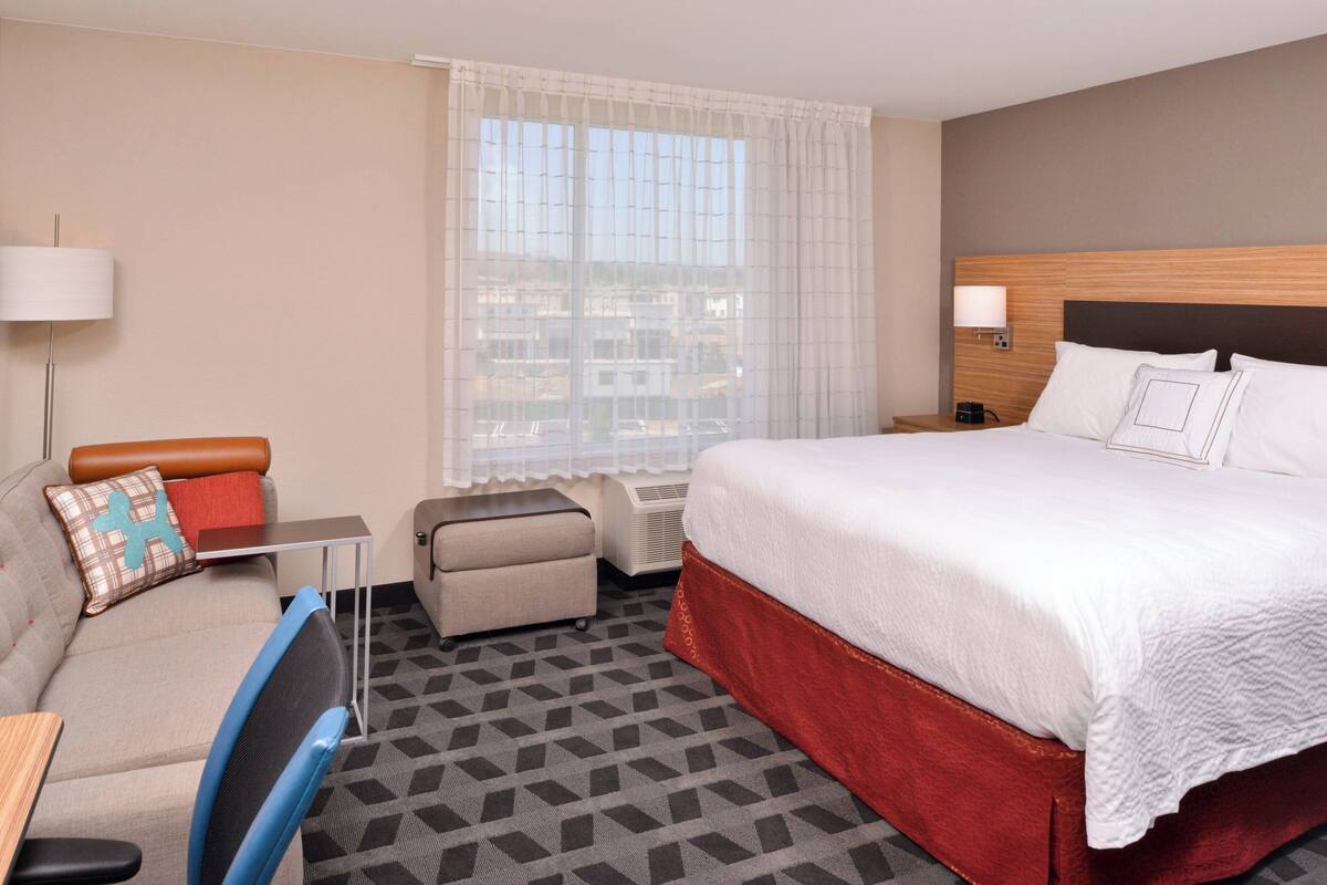 Une chambre d’hôtel avec un grand lit, un canapé, un bureau et une fenêtre donnant sur des immeubles.