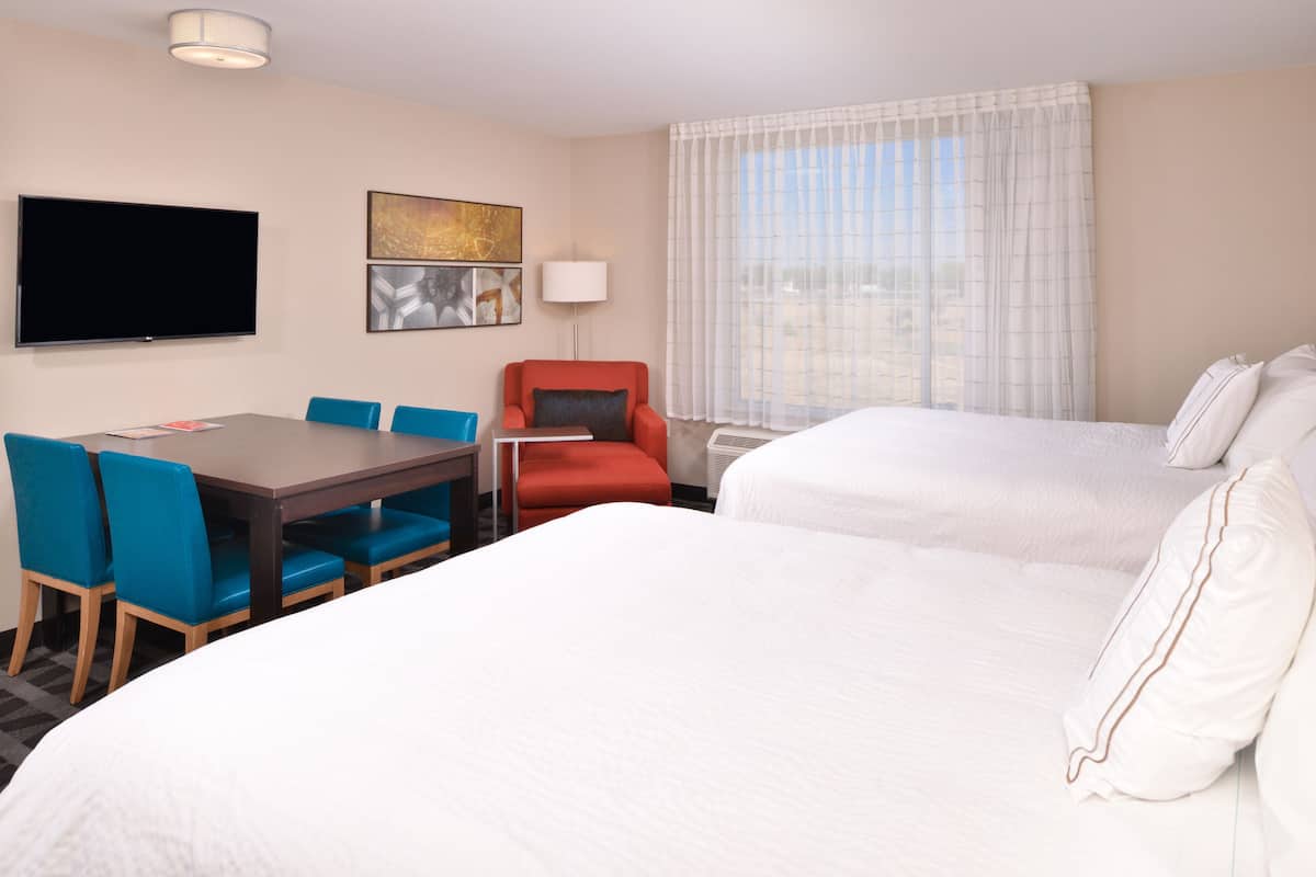 Une chambre d’hôtel comprenant un lit, un bureau avec des chaises, une télévision et une fenêtre avec des rideaux.