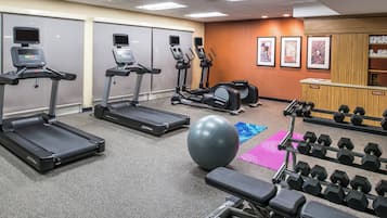 A gym with treadmills, elliptical machines, a stationary bike, a large exercise ball, and a rack of dumbbells.