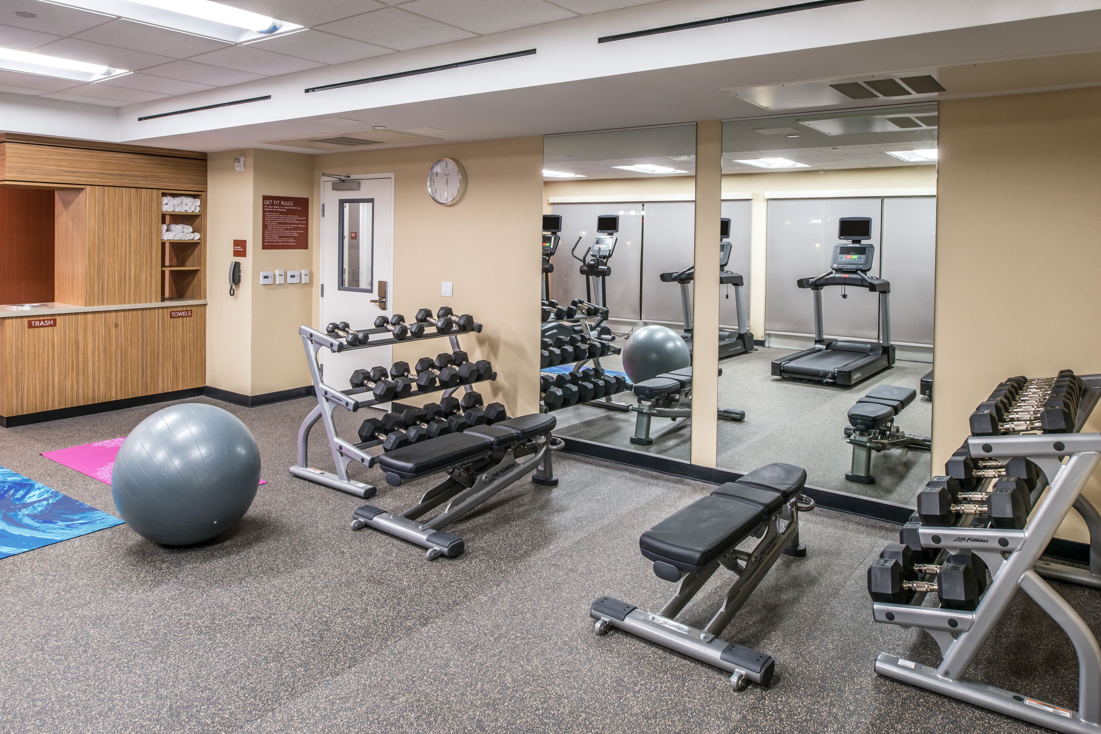 A gym with exercise equipment, a mirror, and a clock on the wall.