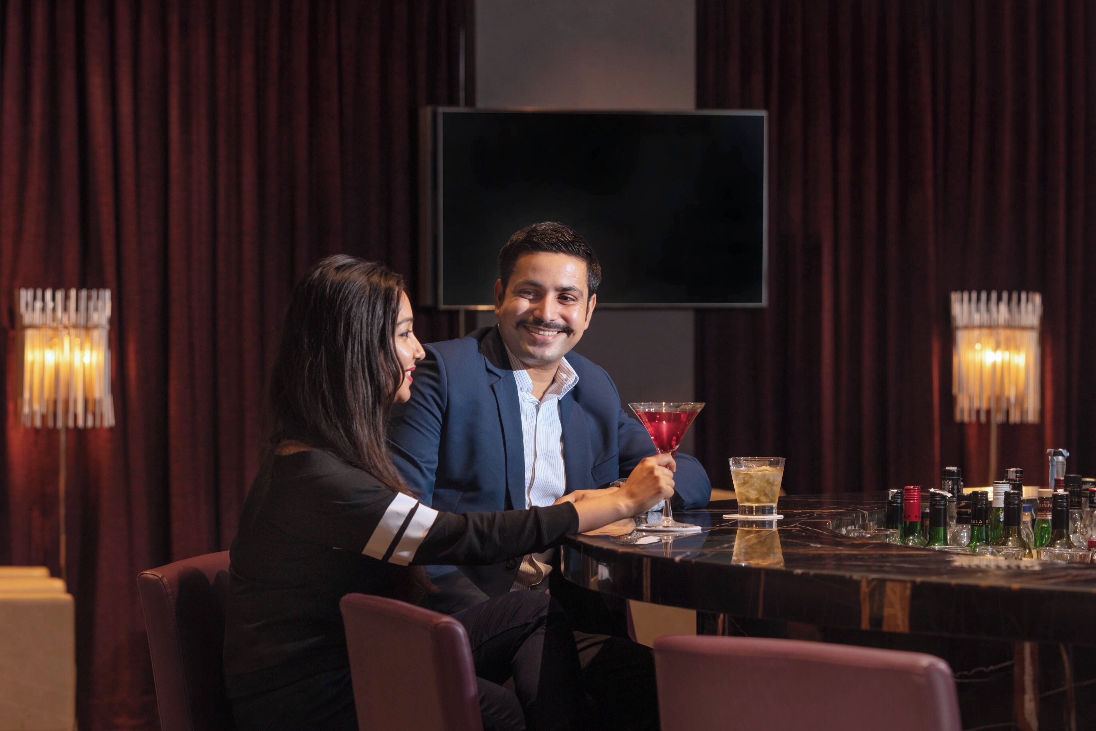 A couple seated at a table in a dimly lit room with a large screen in the background.