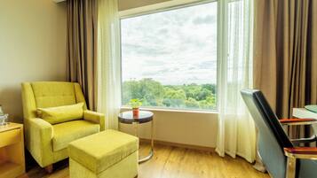 Una habitación con un ventanal amplio, un sillón amarillo, una mesita redonda con una planta y un televisor sobre un mueble bajo.