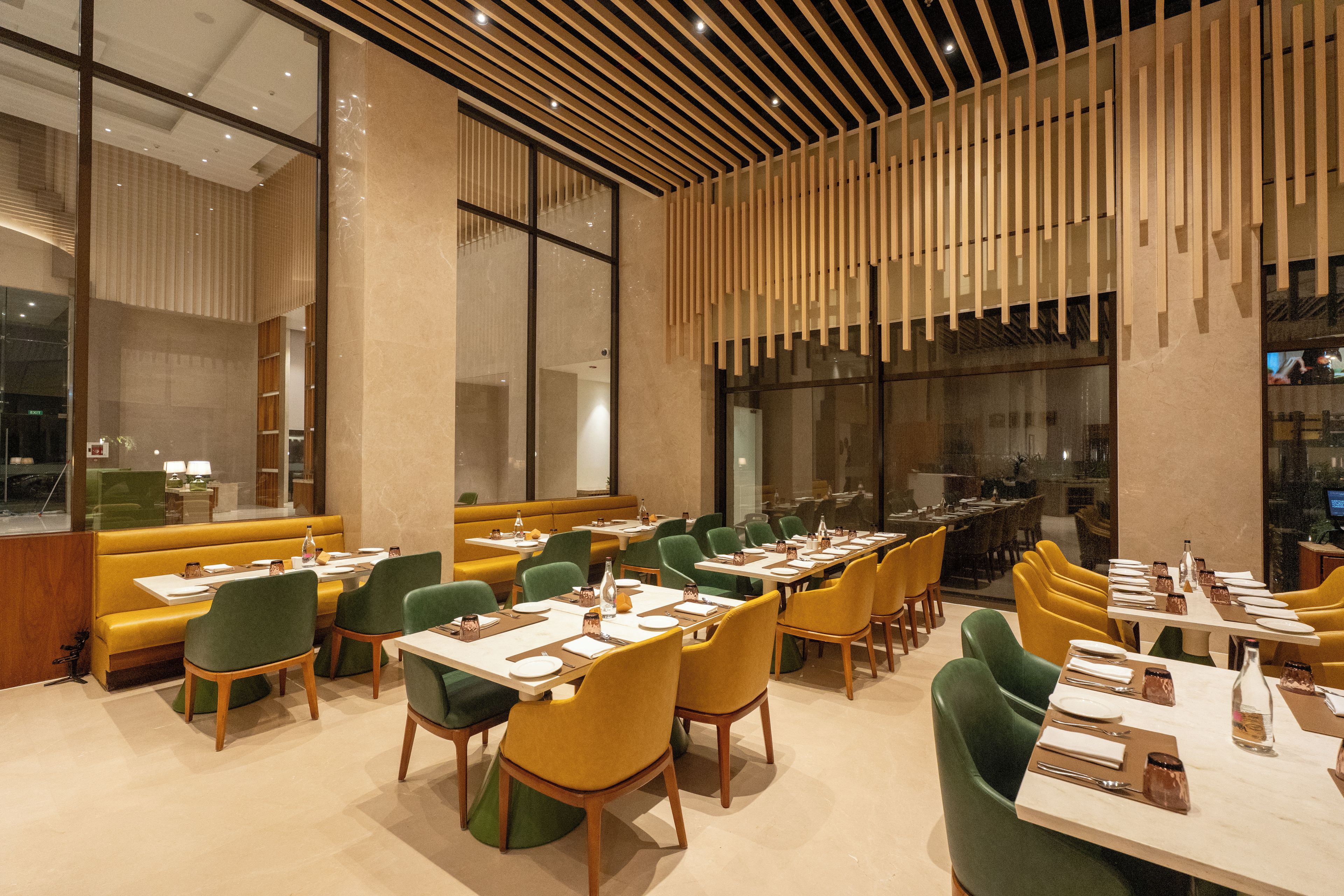 A modern restaurant interior with high ceilings, wooden slats, and a mix of green and yellow seating.