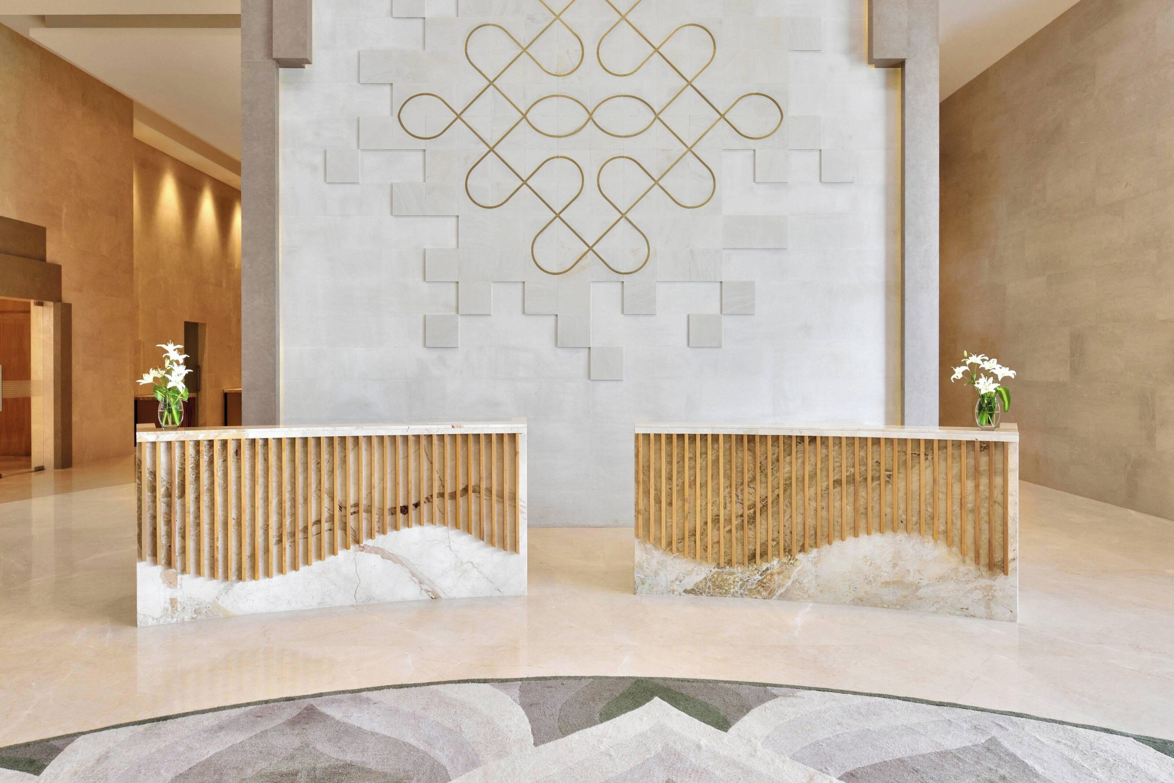 Een receptiezone met twee houten balies, een marmeren vloer en een geometrisch wandontwerp.