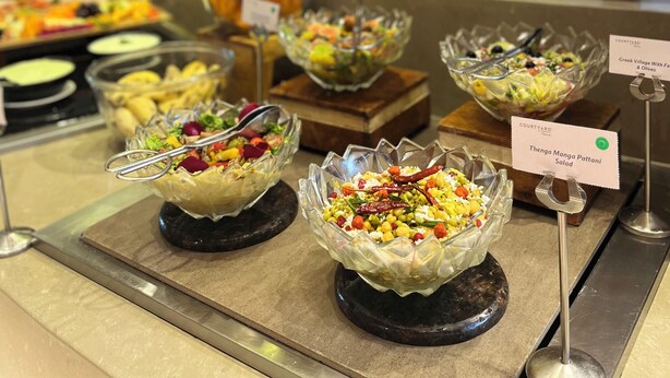 A buffet with various dishes, including a Greek Village salad, a corn salad, and a fruit bowl. - Courtyard by Marriott Madurai (Madurai)