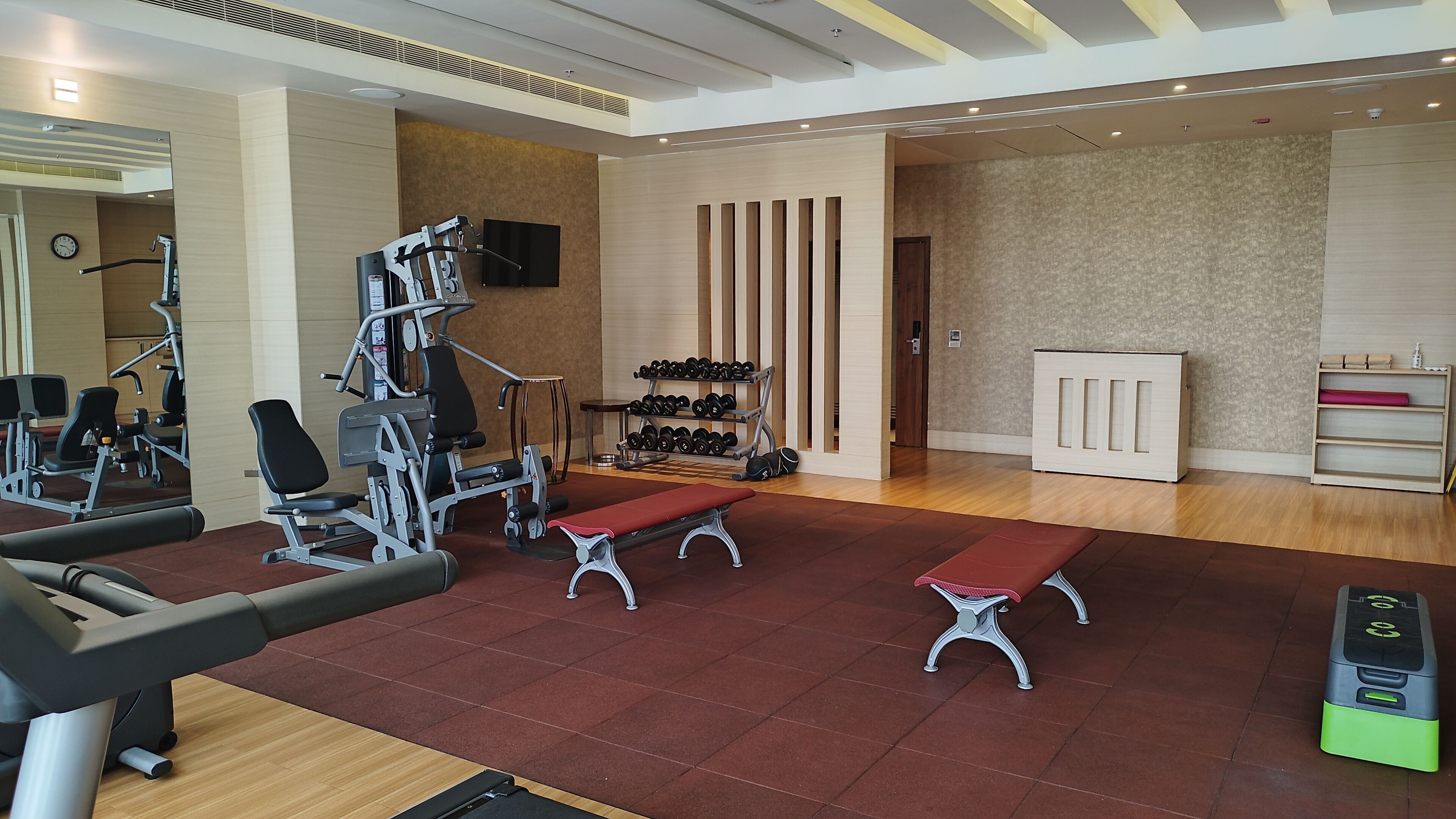 A gym with exercise equipment, benches, and a wall-mounted TV.