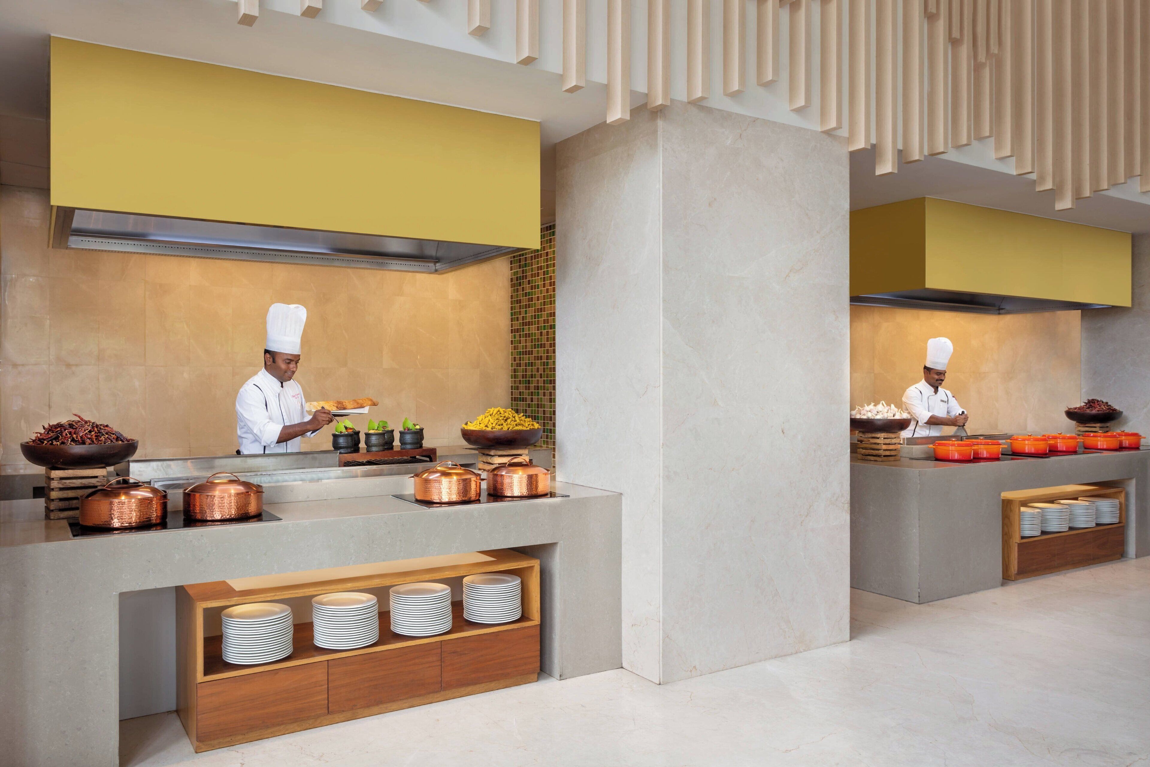 A modern kitchen with chefs preparing food, copper pots, and a buffet setup with plates and bowls.