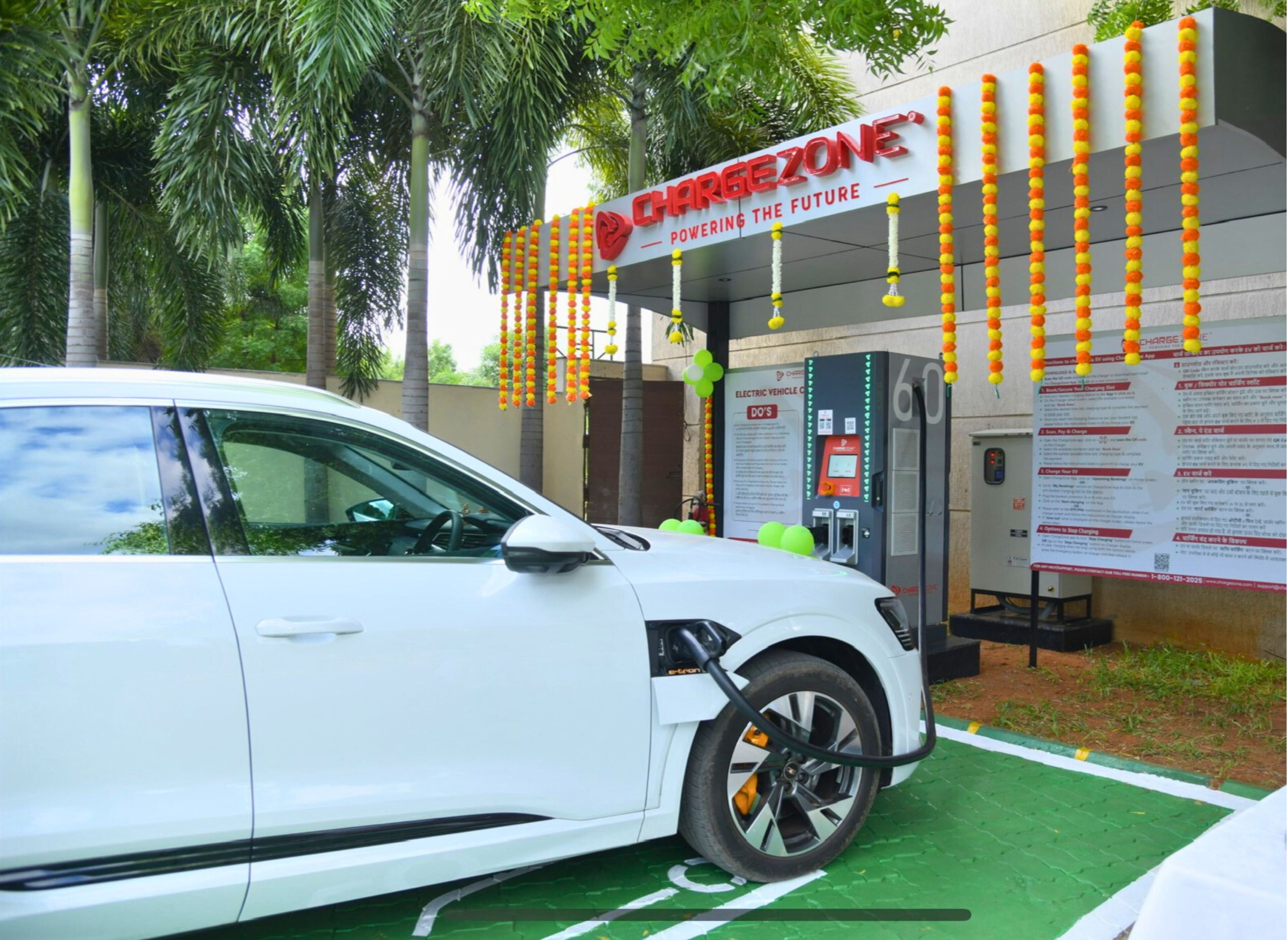 A white car parked at a charging station with a sign reading "CHARGEZONE" and "POWERING THE FUTURE".