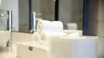 Een witte handdoek op een witte doos in een badkamer met een spiegel en een wastafel.
