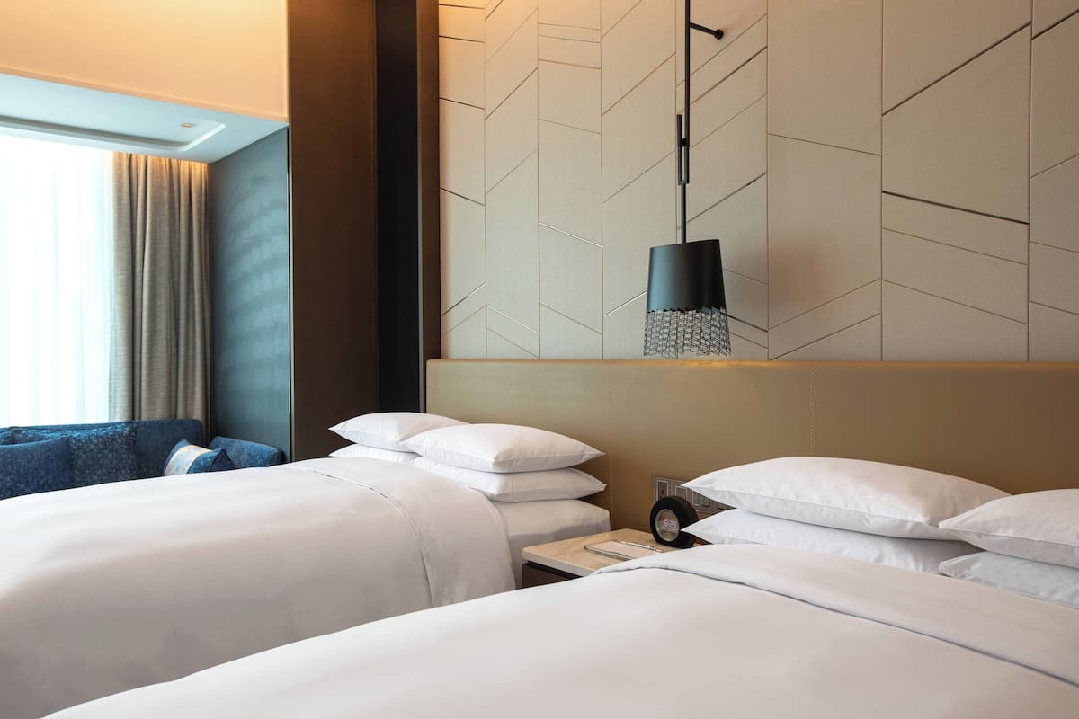 A hotel room with two beds, a large window with curtains, a modern wall design, and a hanging light fixture.